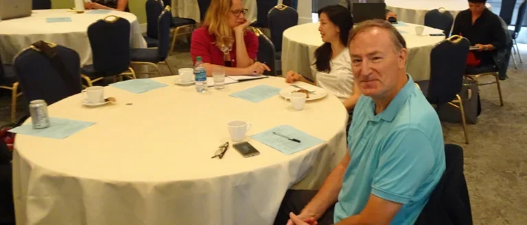 Ron Hays sitting at a table in blue shirt at 2018 Research Symposium.